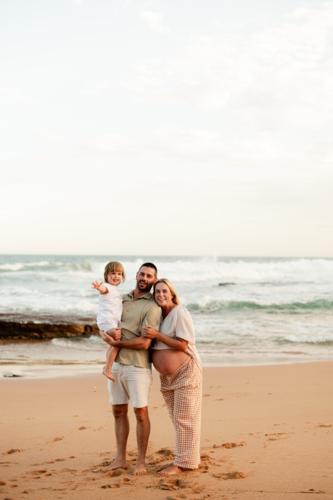 Family enjoying sunset on a beach with expecting mother and playful child - Australian Stock Image