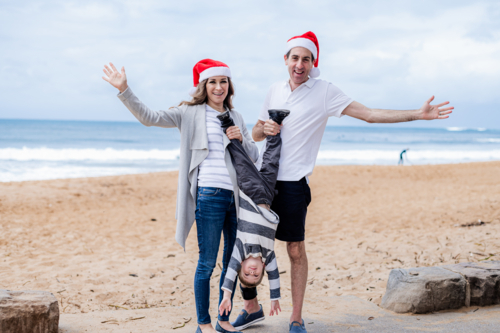 Family joyfully celebrating Christmas on the beach, wearing Santa hats - Australian Stock Image
