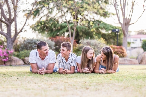 Family lying together on grass looking at each other and laughing - Australian Stock Image