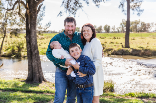 Family of four happy and smiling near river with green grass - Australian Stock Image
