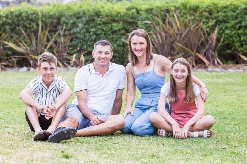 Family of four sitting together in garden smiling - Australian Stock Image