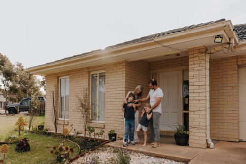 Family of four standing in front of their house. - Australian Stock Image