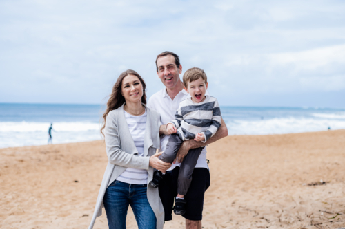 Family of three happy on a sandy beach with ocean waves in the background - Australian Stock Image