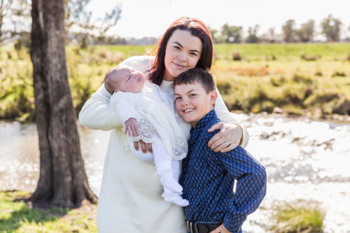 Family of three mum, son and newborn baby girl cuddling and happy near river - Australian Stock Image