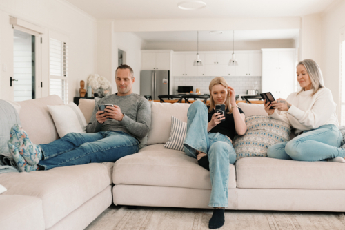 Family of three sitting comfortably on the couch while on their phones - Australian Stock Image