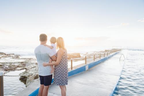 Family of three watching the sunrise at the beach - Australian Stock Image