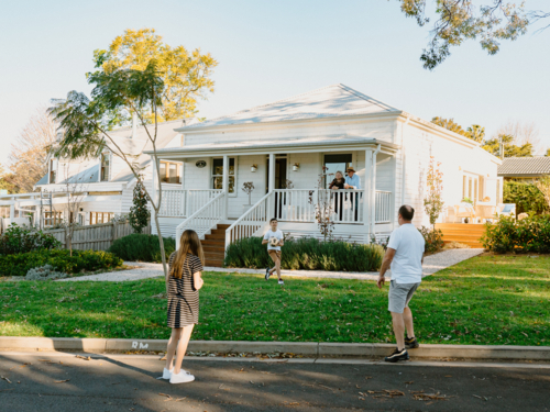 Family playing soccer in front yard of white weatherboard home in suburbs - Australian Stock Image