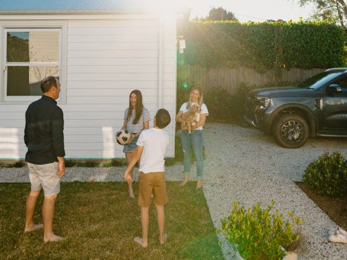 Family playing with a soccer ball in their yard. - Australian Stock Image