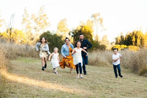 Family running in park, parents chasing children - Australian Stock Image