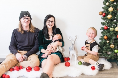 Family sitting together on rug with Christmas decorations and tree - Australian Stock Image