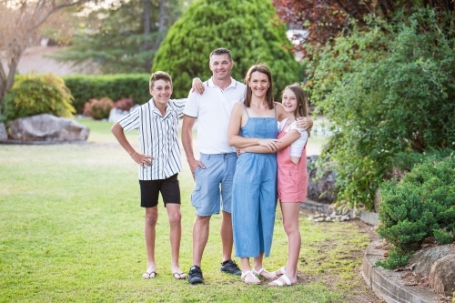 Family standing together mum and daughter hugging son leaning on father - Australian Stock Image