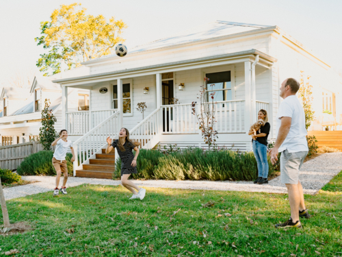 Family tossing a soccer ball inside their yard. - Australian Stock Image