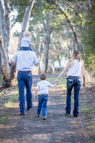 Family walking with baby being carried on father's shoulders while mother holds son's hand - Australian Stock Image