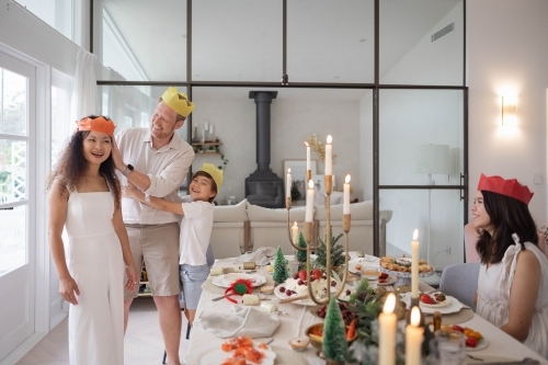 Family wearing paper crowns around Christmas dinner table - Australian Stock Image