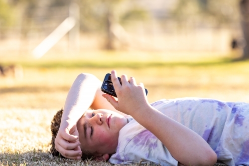 Farm boy lying on grass looking at mobile phone - Australian Stock Image