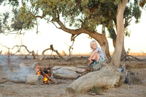 Farm boy sitting on log seat near camp fire in the Australian bush - Australian Stock Image