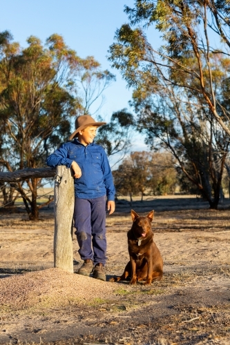 farm kid leaning on post with his red kelpie dog by his side - Australian Stock Image