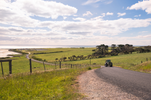 Farm tractor with hay bale driving on the coastal country road. - Australian Stock Image