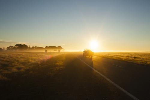Farm ute driving into sun on country highway - Australian Stock Image