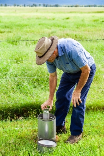 Farmer checking rain gauge after drought has broken and paddocks are green - Australian Stock Image