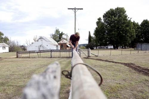 Farmer climbing over fence on a rural property - Australian Stock Image