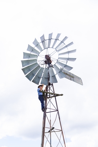 Farmer climbing up farm windmill to check and repair pump - Australian Stock Image