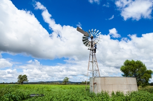 Farmer climbing up farm windmill to check and repair pump - Australian Stock Image