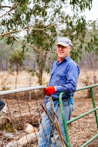 Farmer doing quick repair on broken fence with old gates and wire - Australian Stock Image