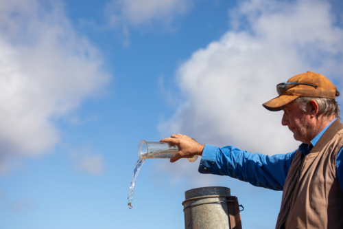 Farmer/grazier tipping water out of a rain gauge - Australian Stock Image