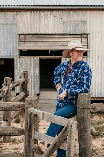 Farmer leans against stock yard fence. - Australian Stock Image