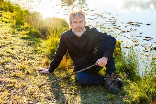 Farmer resting on grass beside dam in paddock - Australian Stock Image