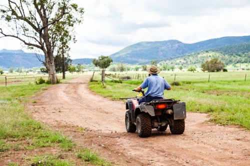 Farmer riding quad bike down farm driveway over cattle grid - Australian Stock Image