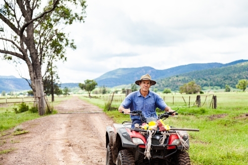 Farmer riding quad bike down farm driveway over cattle grid - Australian Stock Image