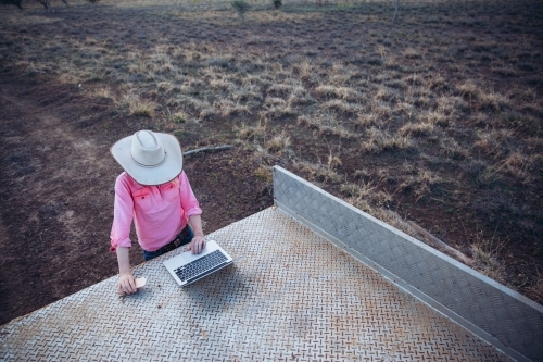 Farmer using laptop in tray of vehicle - Australian Stock Image