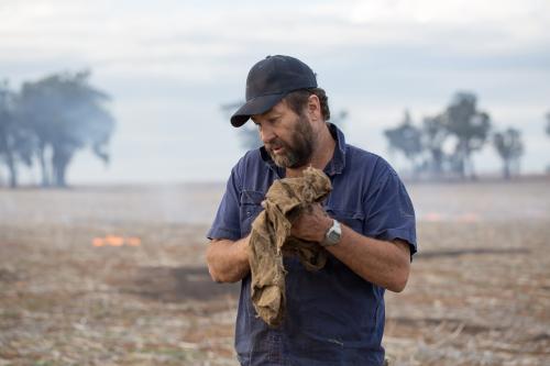 Farmer wiping hands on dirty cloth with burning stubble in background