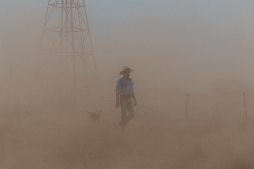Farmer & working dog in the dust with windmill - Australian Stock Image