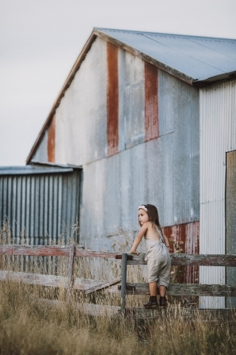 Fashionable young girl climbing a fence in a rural farm setting - Australian Stock Image