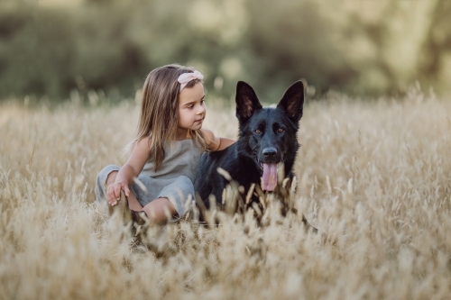 Fashionable young girl, patting a black dog in a farm setting - Australian Stock Image
