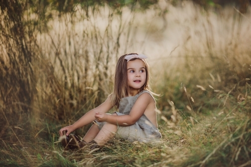 Fashionable young girl, sitting amongst long grass in a farm setting - Australian Stock Image