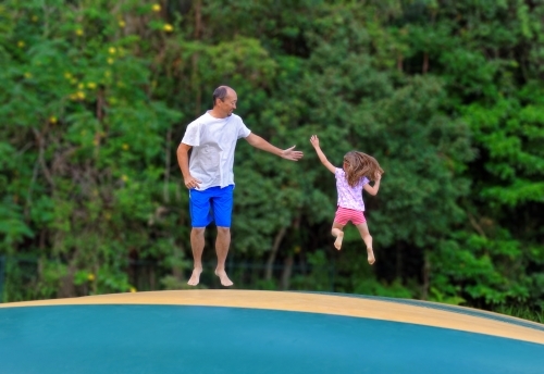 Father and daughter jumping on a jumping pillow having fun together - Australian Stock Image