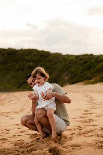 Father and daughter playing together at sunset on a sandy beach - Australian Stock Image