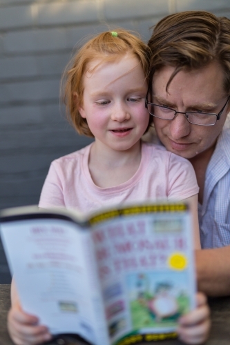 Father and daughter reading a book together outdoors - Australian Stock Image