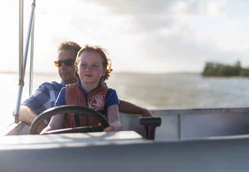 Father and daughter steering a boat together - Australian Stock Image