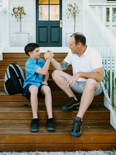 Father and son doing arm wrestling while sitting on the steps of their house. - Australian Stock Image