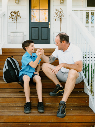Father and son doing arm wrestling while sitting on the steps of their house. - Australian Stock Image