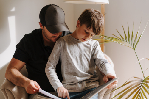 Father and son looking at an album while sitting on the couch. - Australian Stock Image