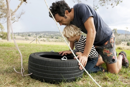 Father and son making a tyre swing in country backyard