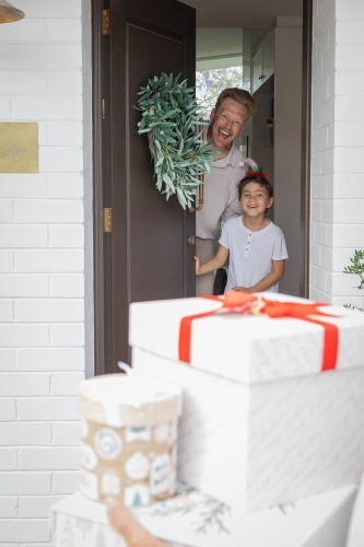 Father and son opening door with wreath to see Christmas presents - Australian Stock Image
