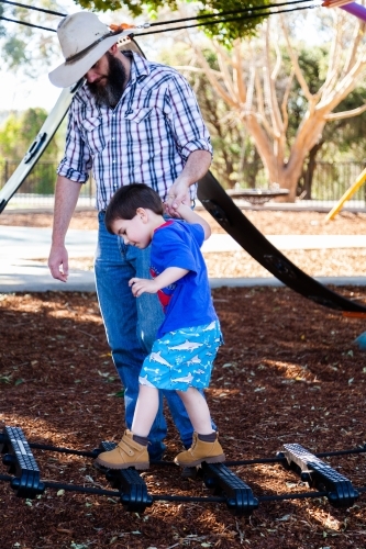 Father and son playing at park outside holding hands helping cross equipment - Australian Stock Image