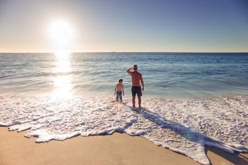 Father and son playing in the waves at the beach at sunset in summer